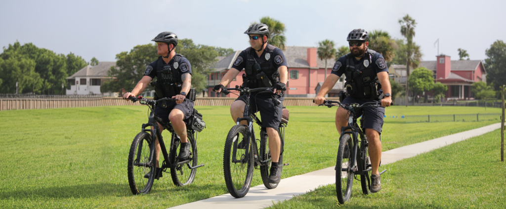 3 Uniformed St. Augustine Police Officers riding their police bicycles on the Castillo de San Marcos fort grounds.