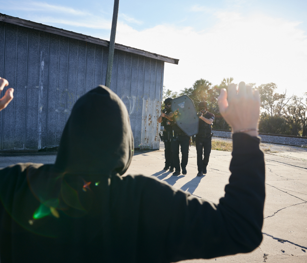 3 Armed Policeman, One with shield covering and 2 with guns.